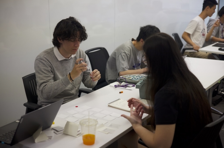 Tisch Summer High School Game Design students sit at a table in a classroom working on game projects